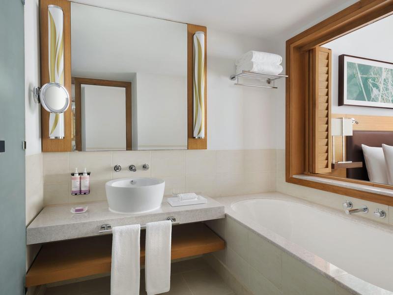 Salle de bain d'hôtel moderne avec baignoire, lavabo, miroir et serviettes.