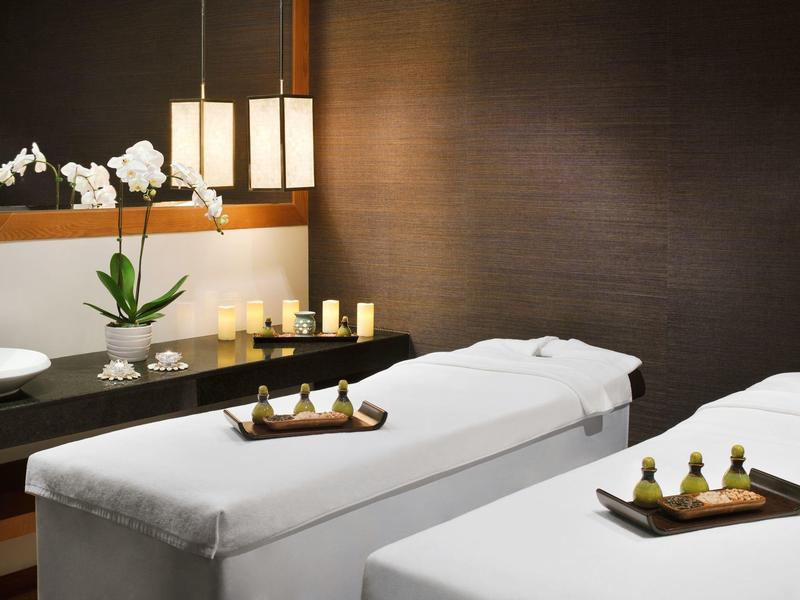 Salles de soins spa modernes avec tables de massage blanches, bougies et orchidées.