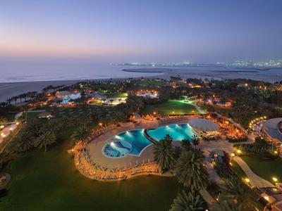 Un complexe hôtelier éclairé avec piscine et vue sur la mer au crépuscule.