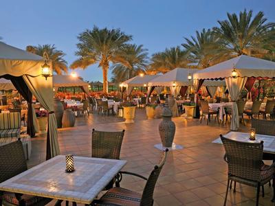 Outdoor hotel area with tables, chairs, umbrellas, and palm trees at dusk.