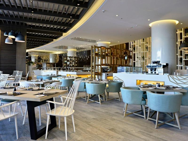 Espace de restaurant d'hôtel moderne avec tables, chaises et couverts mis en place.