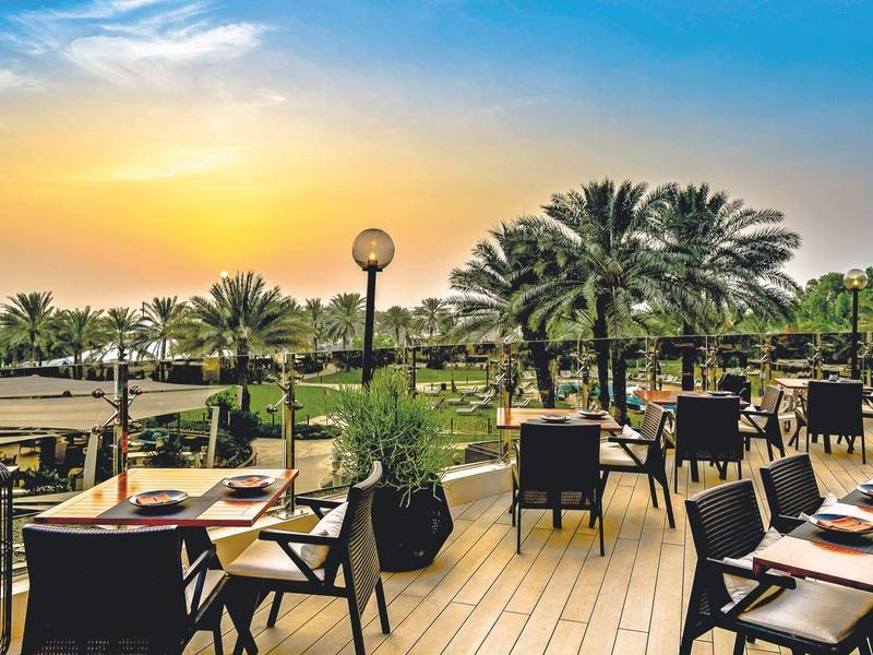 Terrasse d'hôtel avec tables, chaises et palmiers au coucher du soleil.