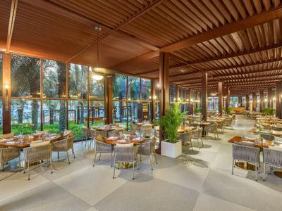 Helles, modernes Restaurant mit Holzdecke, vielen Tischen und Blick auf beleuchtete Gartenanlage.