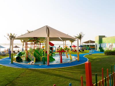 Moderner Kinderspielplatz mit Wasseranlagen und schattigem Pavillon in einer Hotelanlage am Meer.