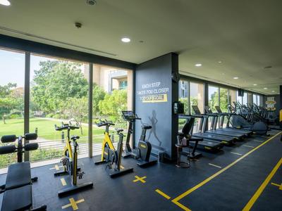 Fitnessraum mit verschiedenen Trainingsgeräten und großen Fenstern mit Blick auf den Garten.