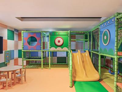 Bunte Kinderspielecke mit Rutsche, Klettergerüst und Tischen in einem Innenraum.