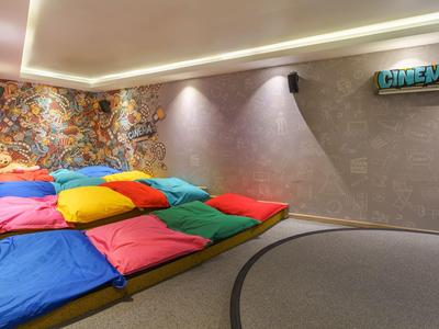 Ein farbenfroher Kinoraum mit breiten Sitzkissen und schummrigem Licht in einem Hotel.