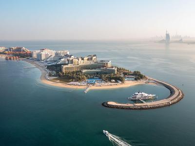 Luxuriöse Inselanlage mit Hotel, Strand und Yachthafen in ruhigem Meerwasser.
