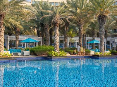 Ein klarer, blauer Pool umgeben von Palmen und Sitzbereichen im Freien eines Hotels.