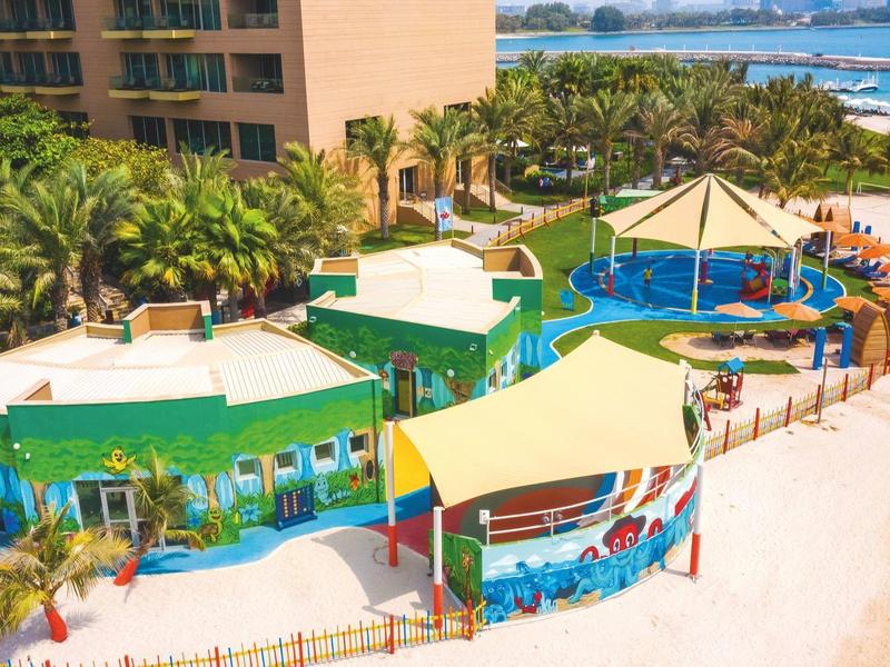 Bunte Strandbungalows neben einem Hotel mit Palmen und Meer im Hintergrund.