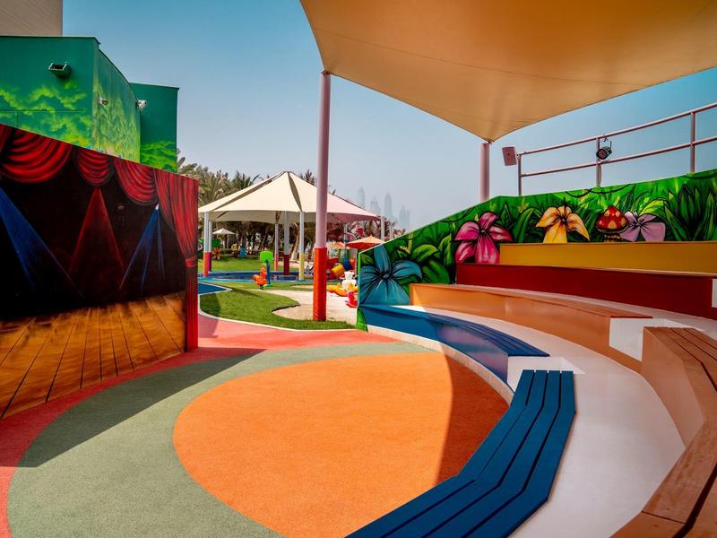 Bunte und überdachte Außenspielanlage mit Sitzstufen und Bühnenbereich.