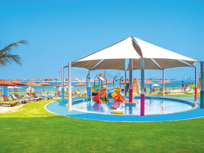 Kinderplantschbecken mit Sonnenschutz und bunten Wasserspielen in einem Ferienresort