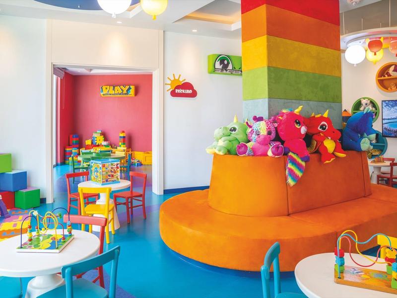 Bunter Kinderspielraum mit orangefarbener Sitzinsel, Spielzeug und Tischen zum Malen und Basteln.