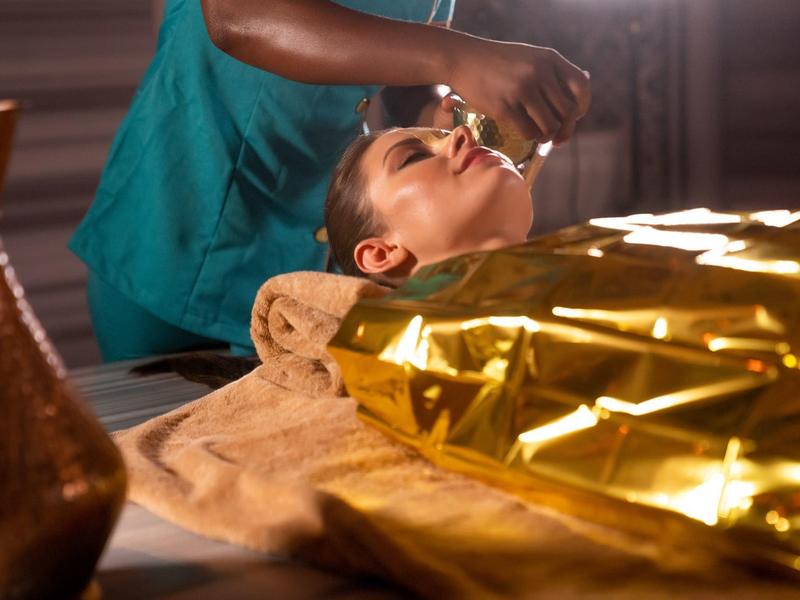 Frau entspannt sich bei einer Gesichtsbehandlung in einem Spa mit goldener Decke.
