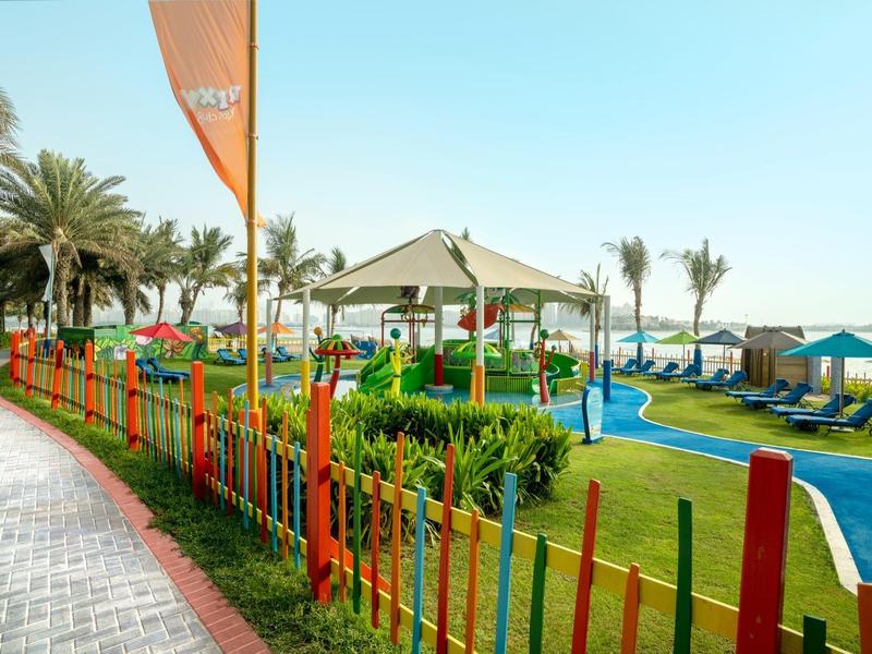 Bunter Zaun entlang eines gepflegten Gartenbereichs mit Pool und Sonnenschirmen.