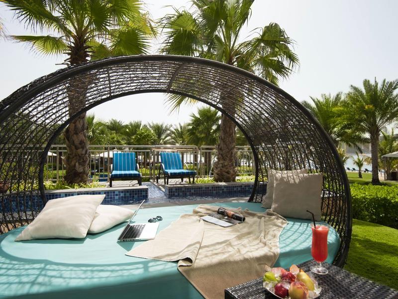 Gemütlicher runder Lounge-Bereich mit Kissen und Getränken in tropischer Gartenanlage.