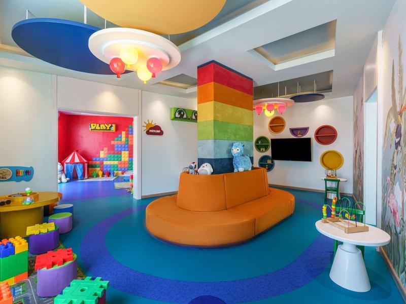 Bunter Kinderspielraum mit weichem orangefarbenem Sitzbereich und Spielzeug auf blauem Boden.