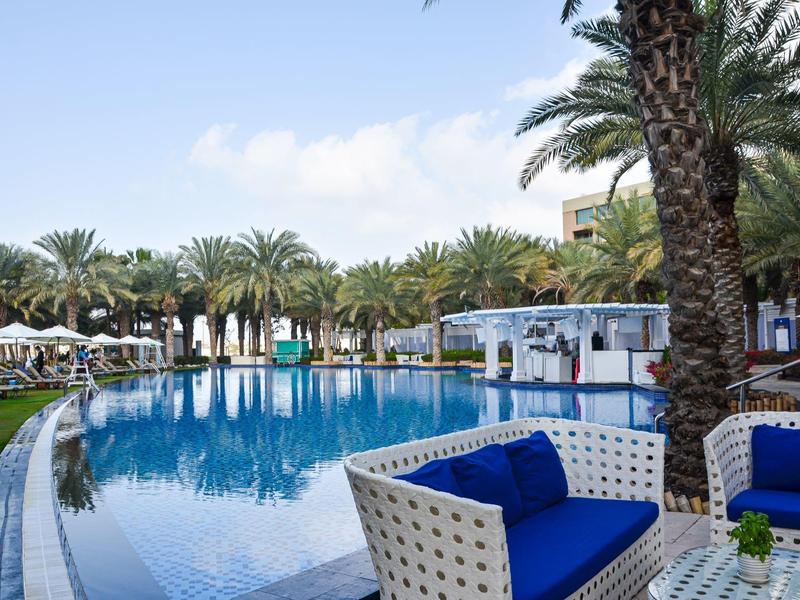 Moderner Poolbereich mit weißen Loungemöbeln und Palmen an einem sonnigen Tag.