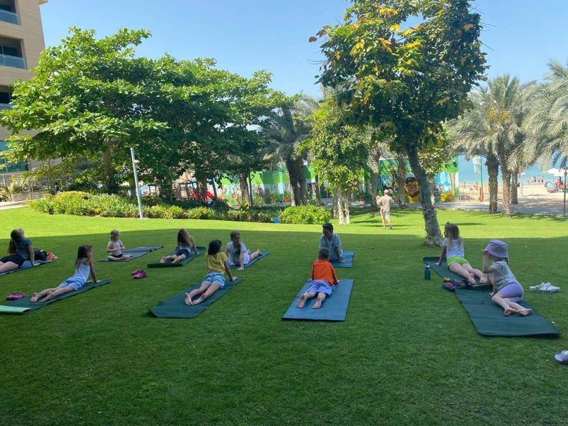 Menschen machen Yoga im Park auf grüner Wiese unter Bäumen bei klarem Himmel.