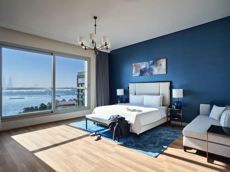 Modernes Hotelzimmer mit großem Bett, blauer Akzentwand und Blick auf das Meer.