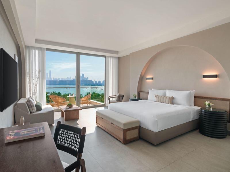 Helles Hotelzimmer mit großem Bett, Schreibtisch und Blick auf eine Stadt und Wasser.