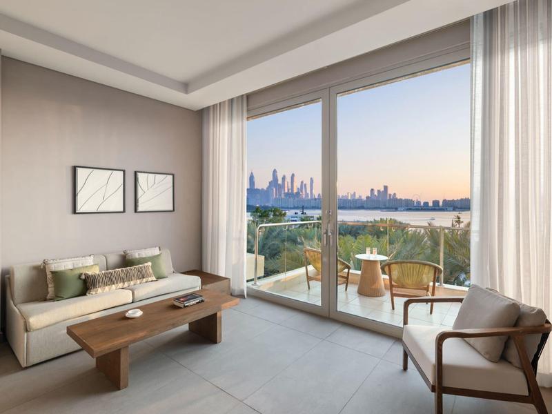 Modernes Wohnzimmer mit Sofa, Sesseln und großer Fensterfront mit Blick auf eine Stadtansicht.