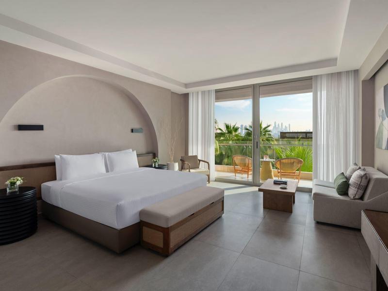 Modernes Hotelzimmer mit großem Bett, Couch und Terrasse mit Blick ins Grüne.