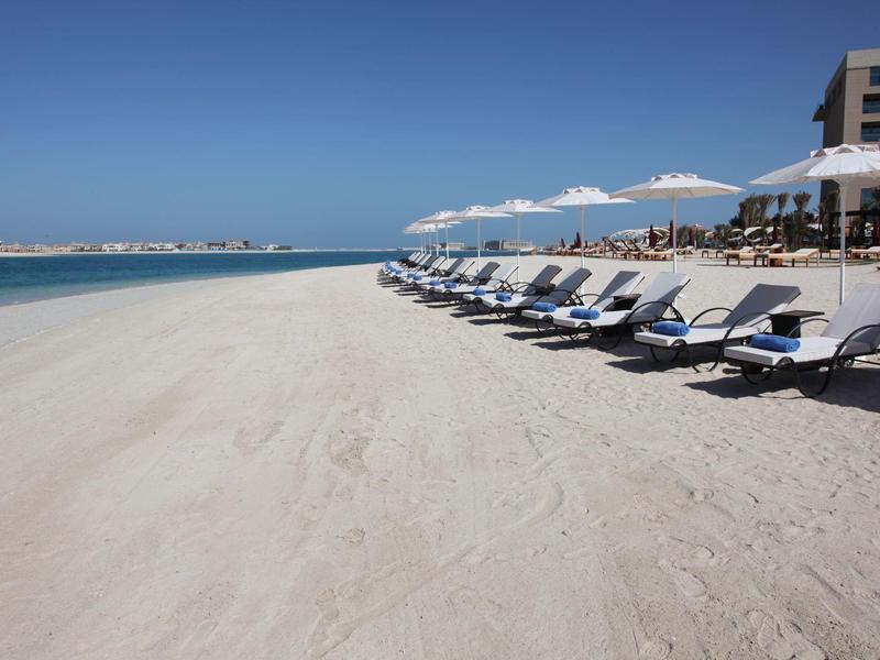 Ein leerer Sandstrand mit einer Reihe von Liegestühlen und Sonnenschirmen neben einem Gebäude.