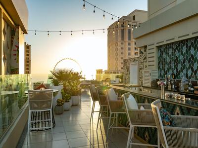 Rooftop terrace with chairs, tables, and a Ferris wheel view at sunset.