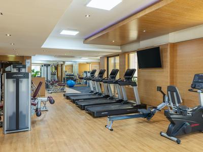 Moderner Fitnessraum mit Holzboden, mehreren Laufbändern, Trainingsgeräten und Wandfernseher.
