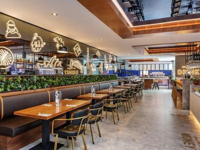 Modern restaurant with wooden tables, black chairs, and neon wall decorations.