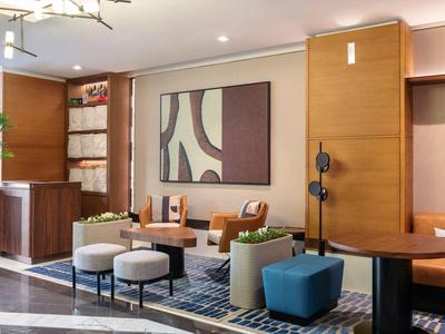 Modern hotel lounge area with wood paneling, armchairs, stools, and abstract wall art
