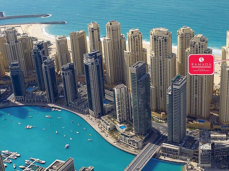 Widok na nowoczesny port z wysokimi drapaczami chmur i jachtami na niebieskiej zatoce wodnej.