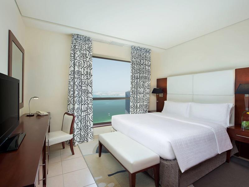 Nowoczesny pokój hotelowy z podwójnym łóżkiem, widokiem na morze i biurkiem z telewizorem.