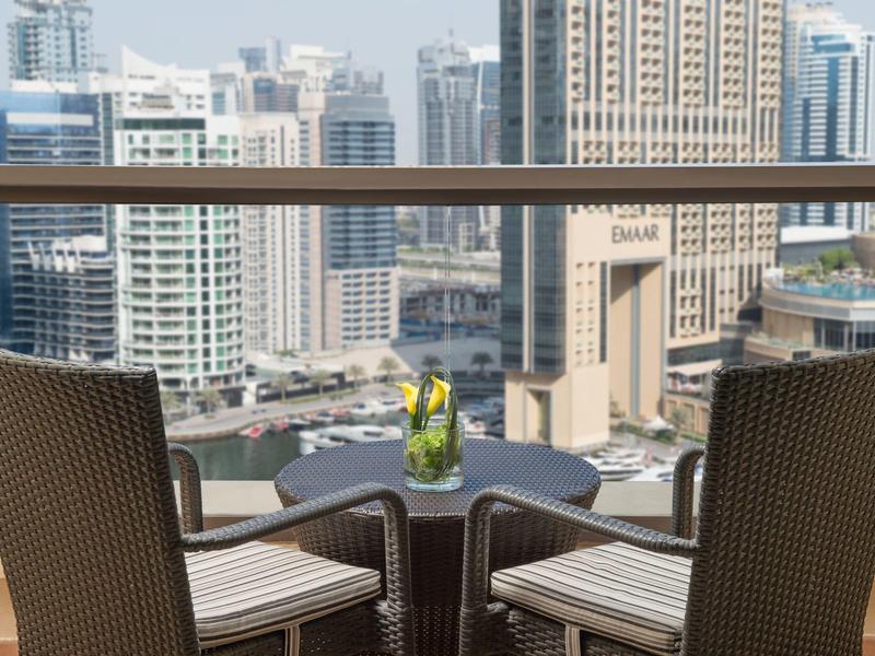 Dwa krzesła i mały stolik na balkonie z widokiem na miasto w świetle dziennym.