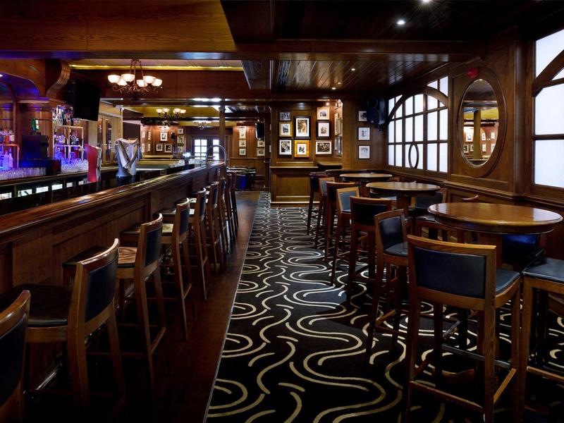 Elegancki bar z ciemnego drewna, stołkami i wzorzystym dywanem przy przyćmionym świetle.