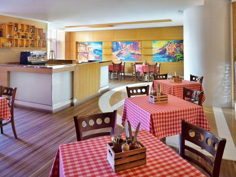 Jasny bar hotelowy z czerwonymi kratkowanymi obrusami i drewnianymi meblami, ozdobiony butelkami wina.