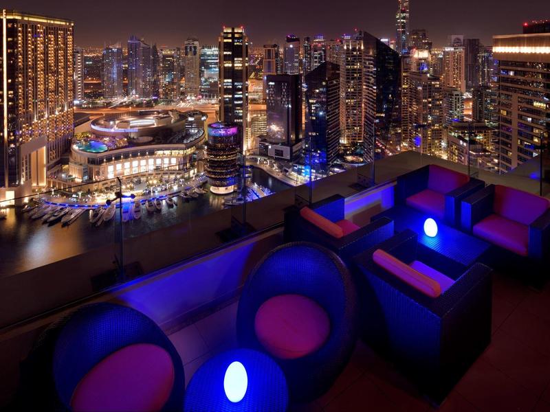 Taras na dachu z nowoczesnym salonem i oświetlonym miejscem do siedzenia, widok na nocne miasto.