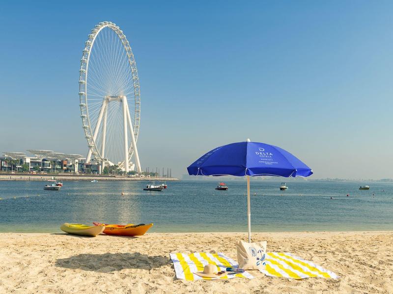 Piaszczysta plaża z ręcznikiem, niebieskim parasolem i dużym diabelskim młynem w tle