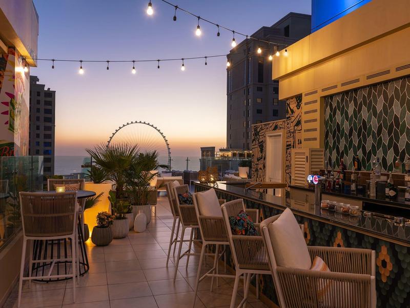 Taras na dachu z wygodnymi miejscami do siedzenia, widok na panoramę miasta i diabelskie koło o zachodzie słońca.