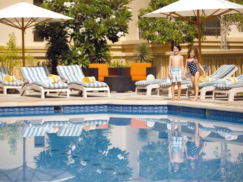 Dwie kobiety przy basenie hotelowym z leżakami i parasolami w tle.