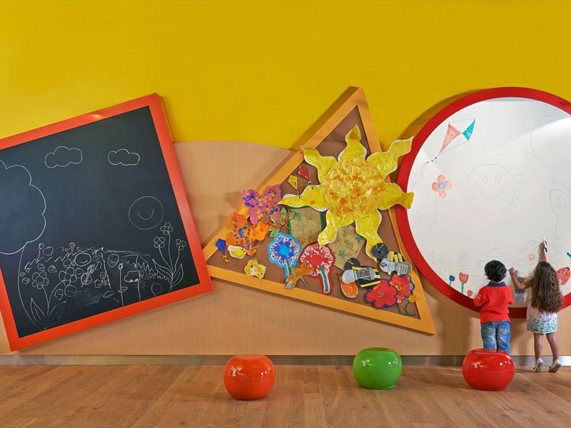 Kinder stehen vor einer großen kreisförmigen Tafel und bunt dekorierten Wand im Spielzimmer.