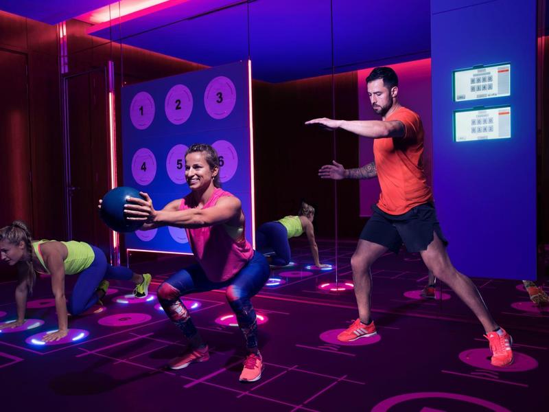 Gruppe trainiert mit Medizinbällen und Dehnübungen in einem neonbeleuchteten Fitnessraum.