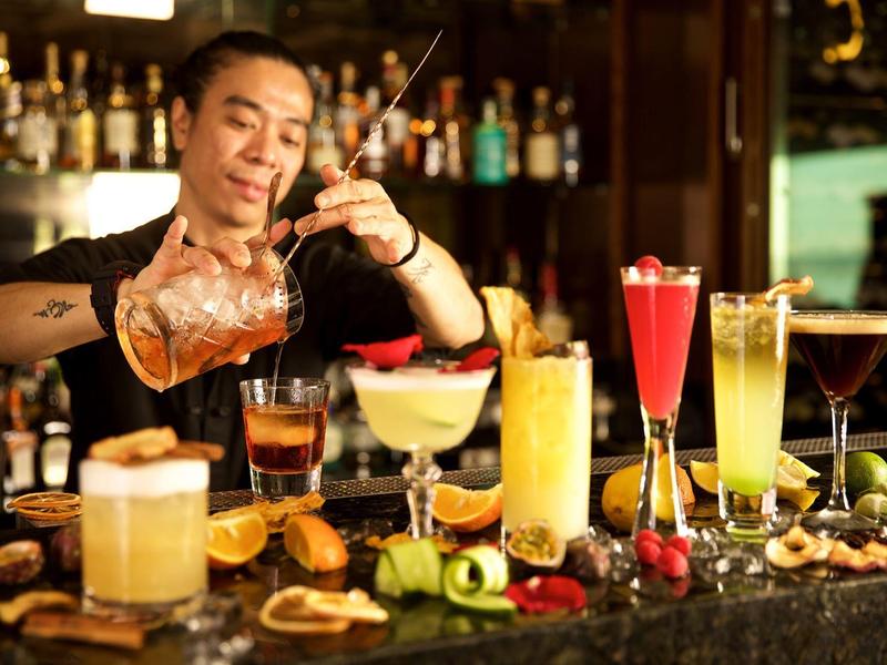 Barkeeper bereitet mehrere bunte Cocktails an einer Bar mit Obst und Garnierungen zu.