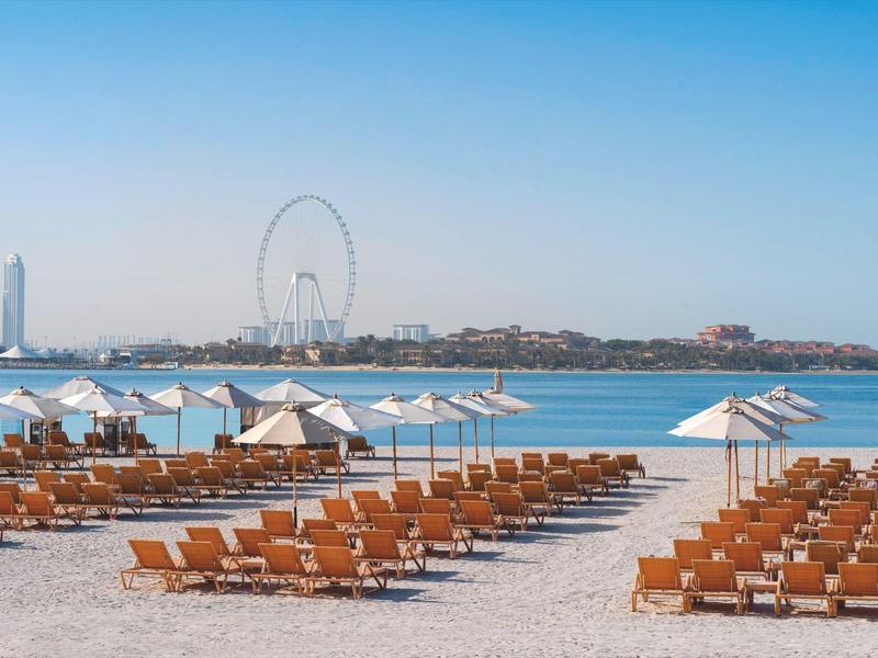 Leerer Sandstrand mit Sonnenliegen und Sonnenschirmen am Meer unter klarem Himmel.