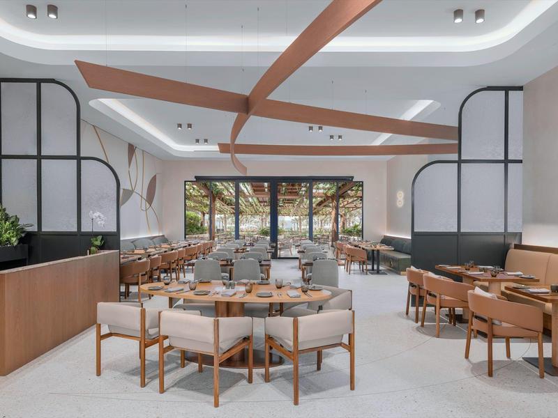 Modernes, helles Hotelrestaurant mit Holzmöbeln und Glasfront zur Terrasse.