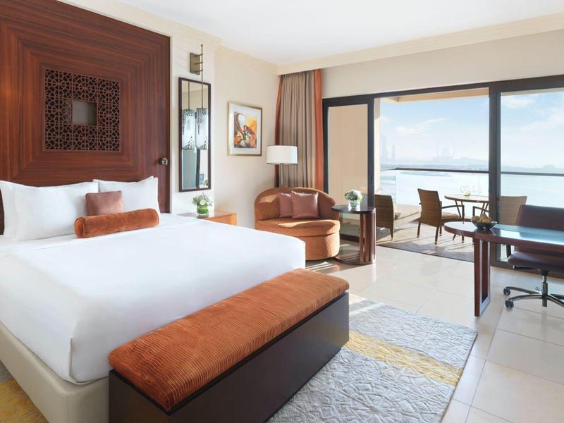 Elegantes Hotelzimmer mit großem Bett, Sitzbereich und Balkon mit Meerblick.