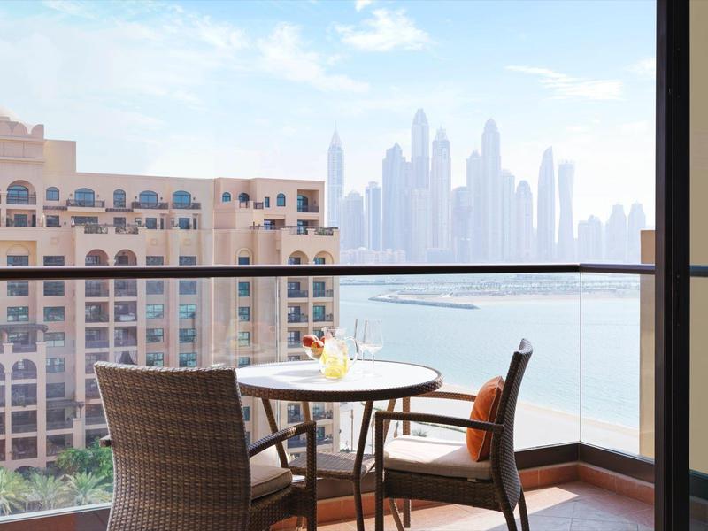 Balkon mit Tisch und Stühlen, Blick auf Stadt und Wolkenkratzer am Wasser.
