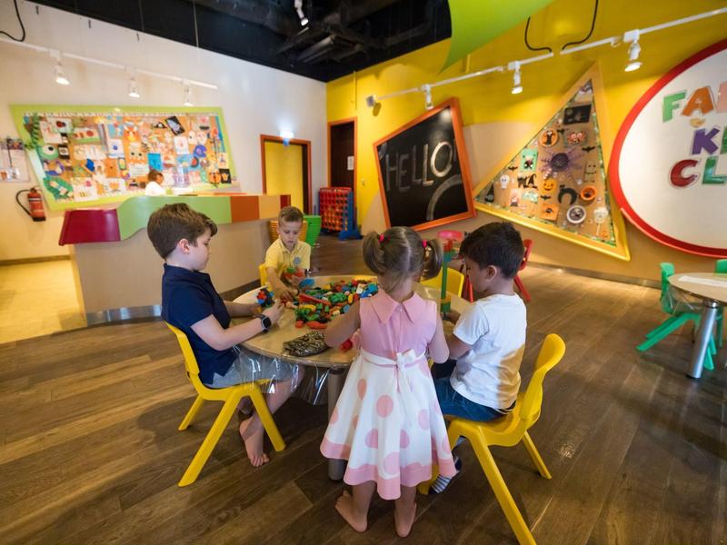 Kinder sitzen um einen Tisch in einem bunten, kinderfreundlichen Raum mit Kunstwerken an den Wänden.