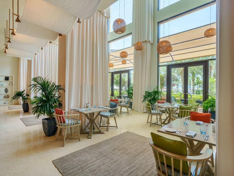 Helles, modernes Restaurant mit großen Fenstern, grünen Pflanzen und gemütlichen Sitzplätzen.